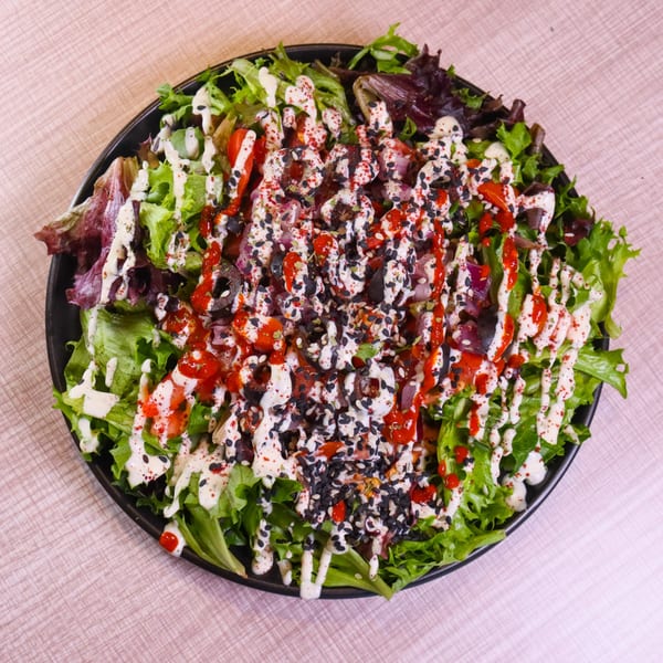 A vibrant salad with mixed greens, red sauce, white dressing, and black sesame seeds in a black bowl.