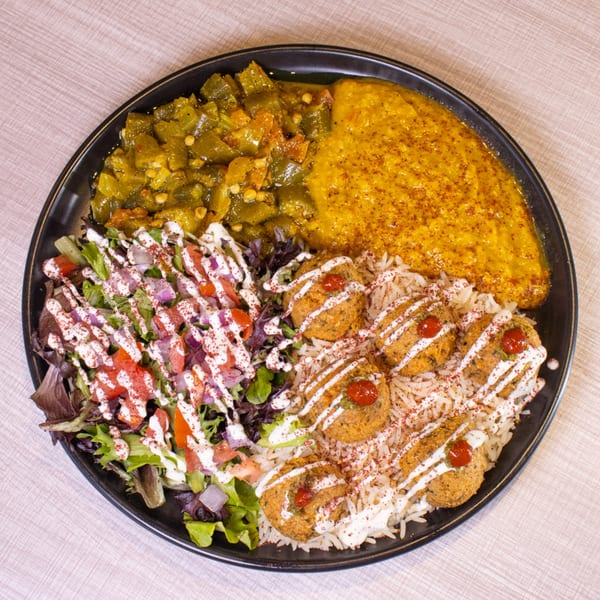 A black plate with falafel, rice, salad, green beans, and yellow lentil stew.