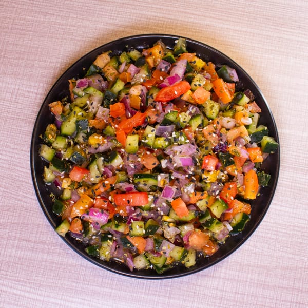 Colorful diced salad with cucumbers, tomatoes, and red onions, topped with sesame seeds.