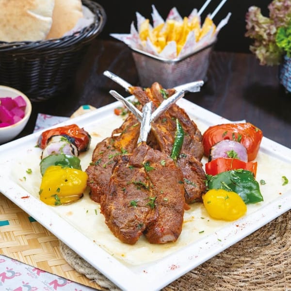 Grilled lamb chops with bell peppers, onions, and tomatoes, served with pita bread and fries.