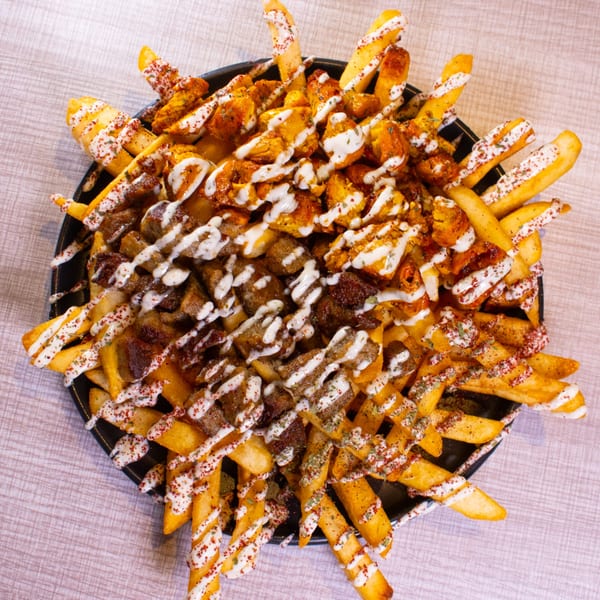 A black plate piled high with golden fries, chicken, beef, white sauce, and red spice.